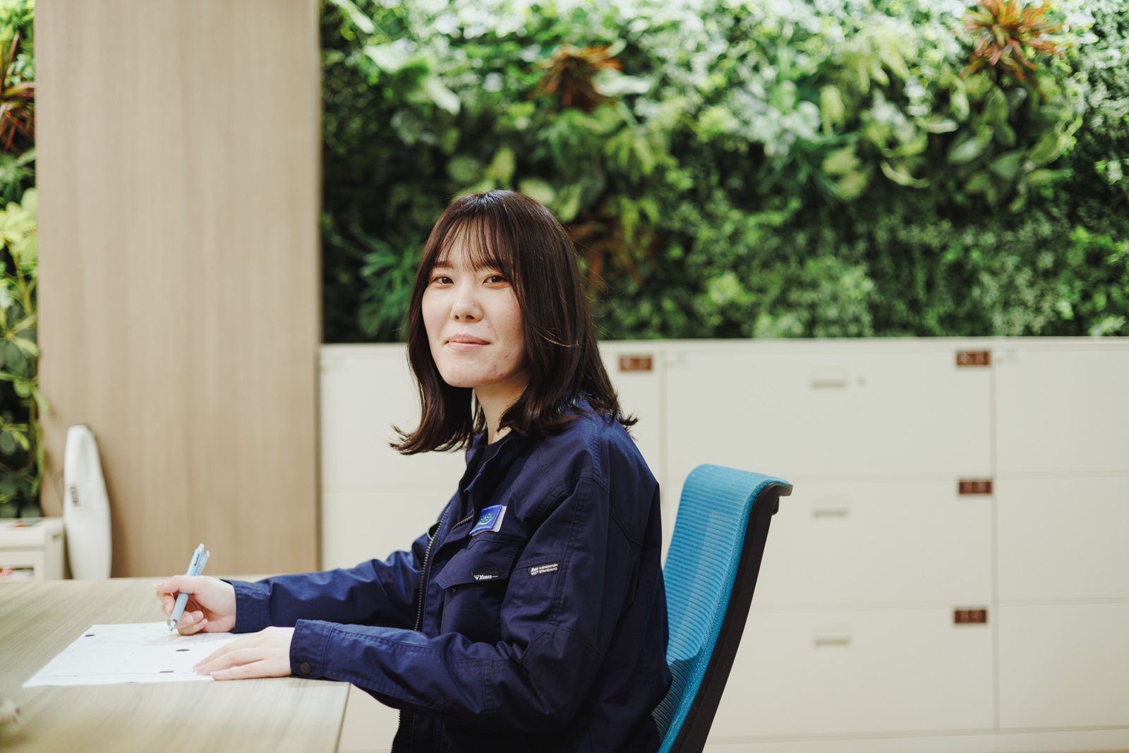 緑の壁面を背にデスクで書き物をする女性スタッフ