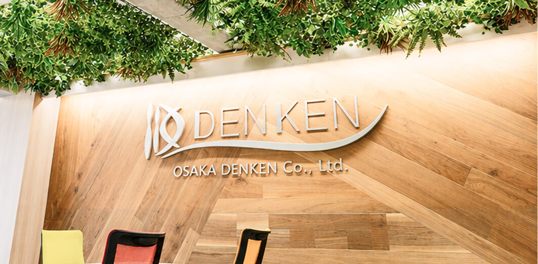 斜め張りの木壁とグリーンを背にしたDENKENのロゴ