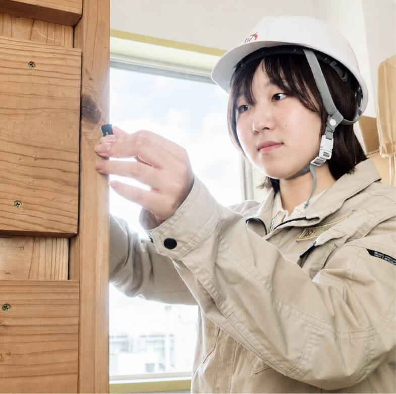 ヘルメットを着用し木製の下地に金具を取り付ける女性スタッフ