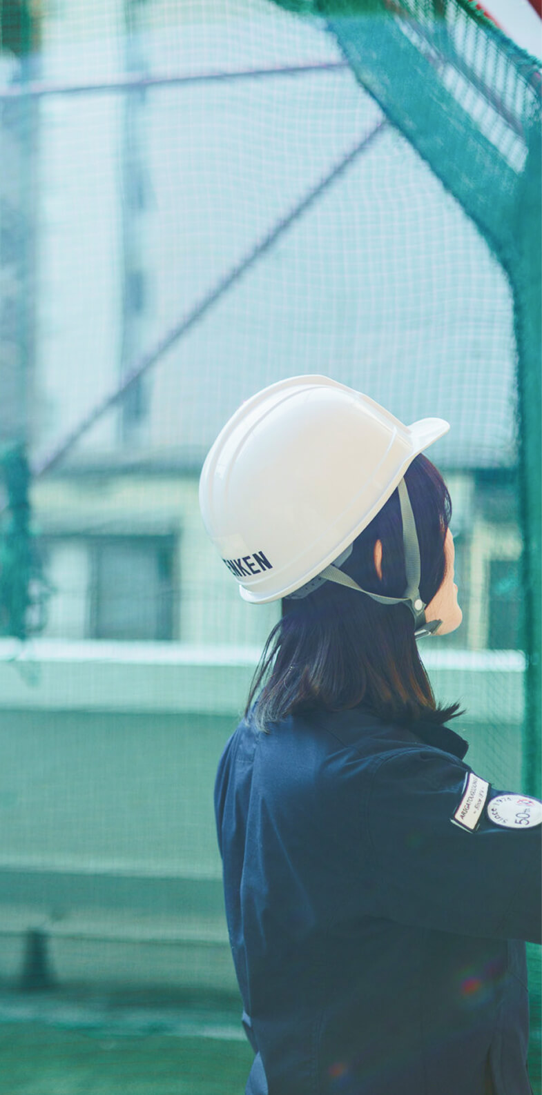 ヘルメットを被り工事現場を見上げる女性スタッフの後ろ姿
